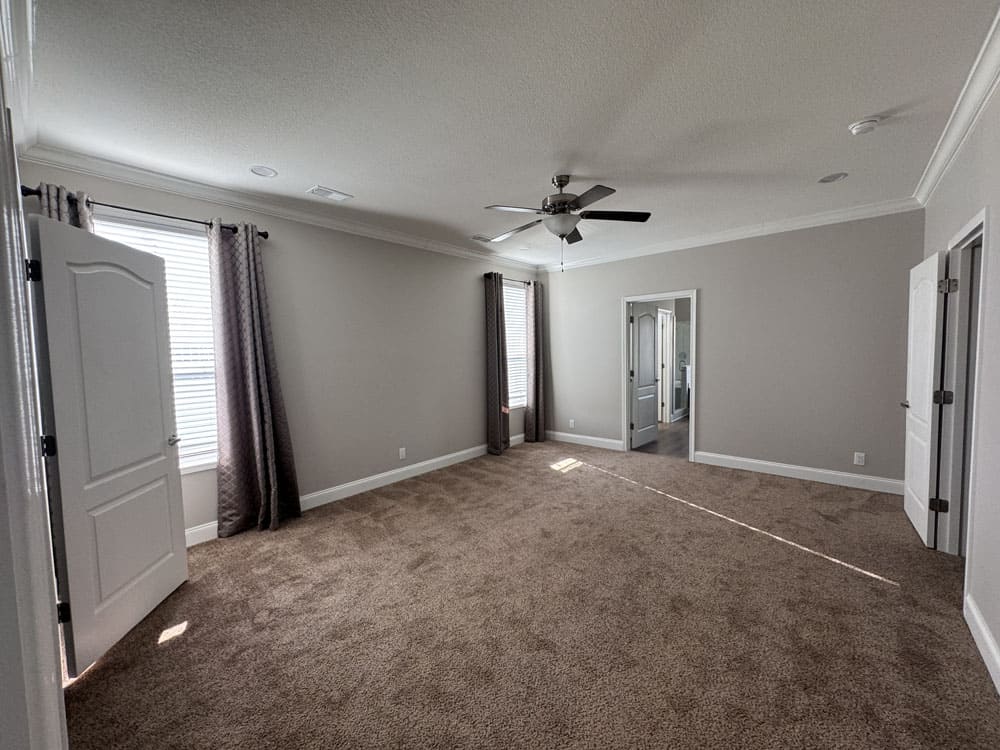Large carpeted primary bedroom with ceiling fan in the 4 bedroom Lilly II modular home near Conroe, Texas