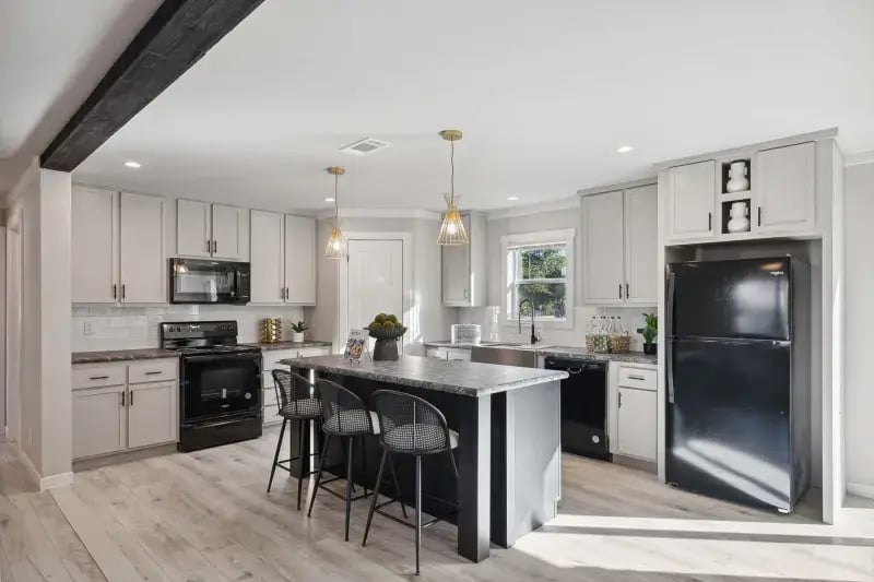 Island kitchen with white cabinets and black appliances in The Carol Champion Homes model