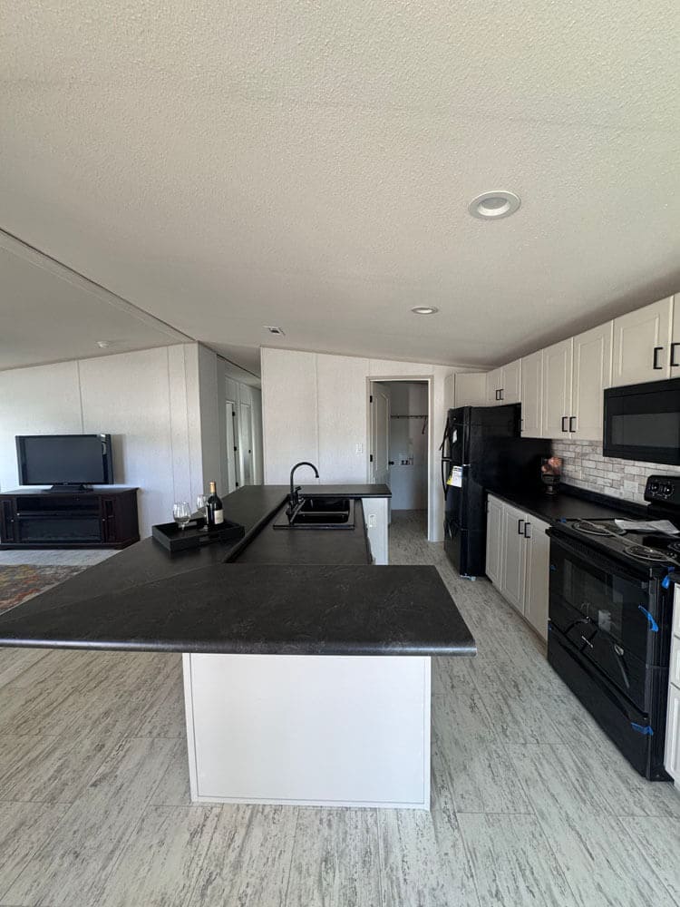 Open-concept kitchen with black appliances in The Lucia mobile home for sale near Conroe