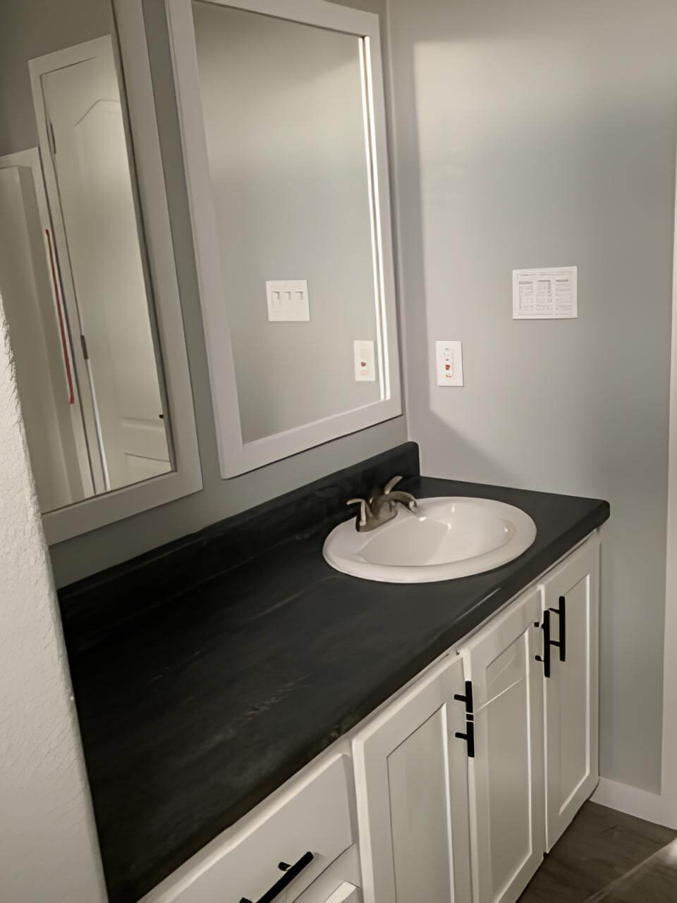 Bathroom vanity with dark countertop and framed mirrors in the Bobby Jo