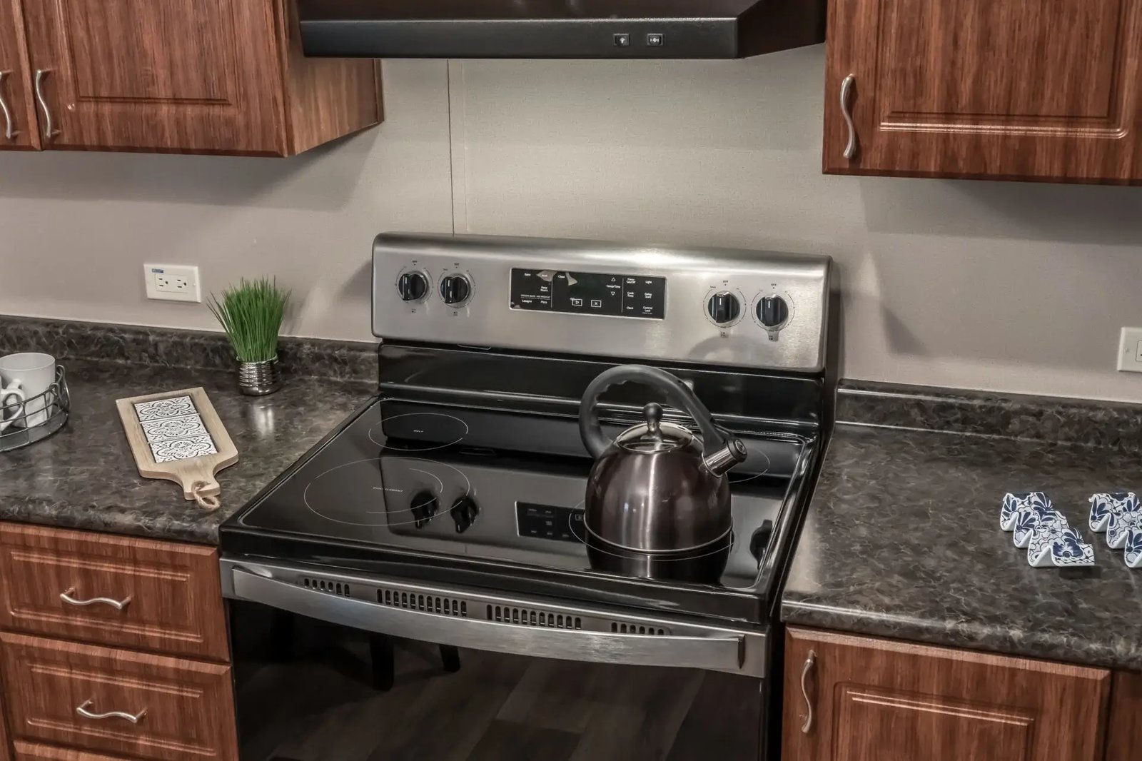 Electric range in The Lisa kitchen with a vent hood, dark stone-look counters, and wood-tone cabinets