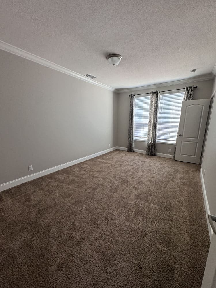 Spacious guest bedroom with plush carpet and double windows in The Lilly II for sale at Premier Homes of Conroe