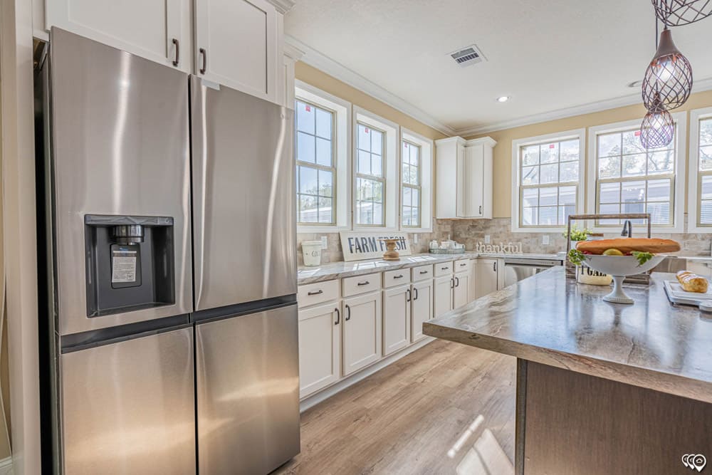Sunlit modular home kitchen with large island and French door refrigerator