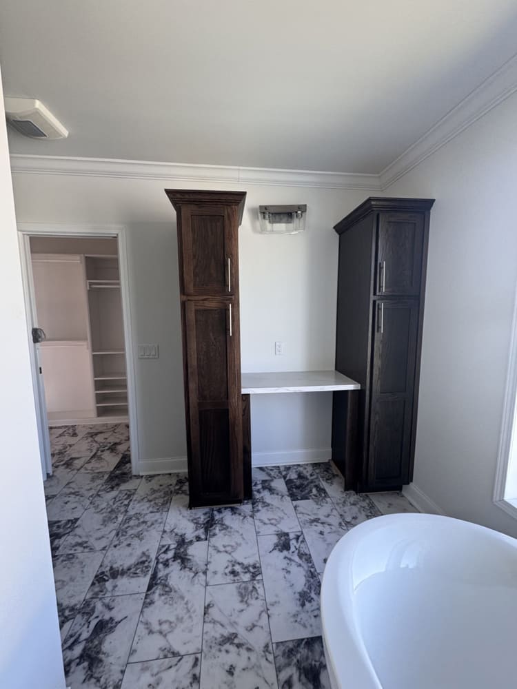 Luxury primary bathroom with linen cabinets, dressing counter and marble-look tile in this Conroe manufactured home