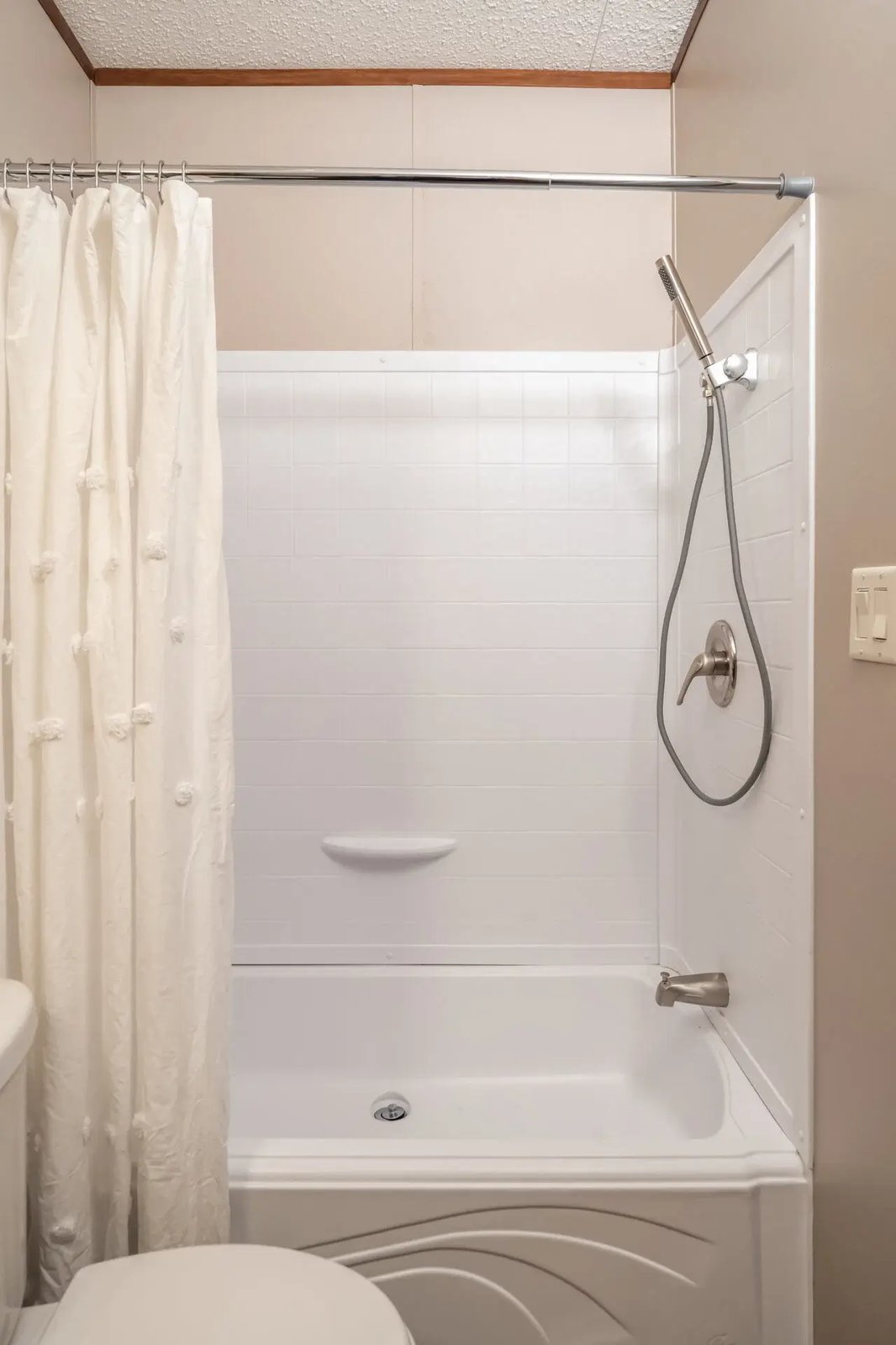 Tub-and-shower combination in The Lisa bathroom with a shower curtain, built-in ledge, and handheld shower fixture