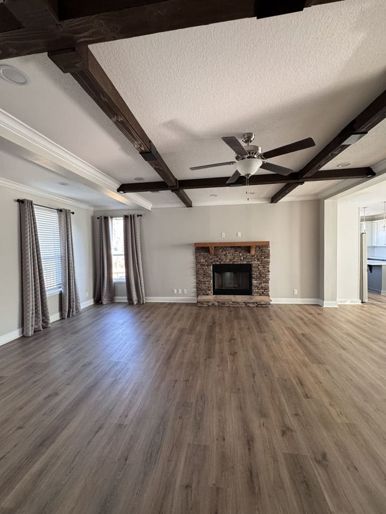 Spacious living area with a stone fireplace, ceiling fan and exposed beams in The Lilly II for sale near Conroe