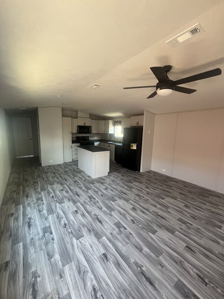 Living area opening to white kitchen cabinets and black appliances in the Legacy FG-H-1664-22A 2-bedroom manufactured home