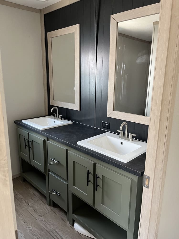 Green double vanity with mirrors and dark accent wall in the Clayton Epic Mariner 3-bedroom manufactured home