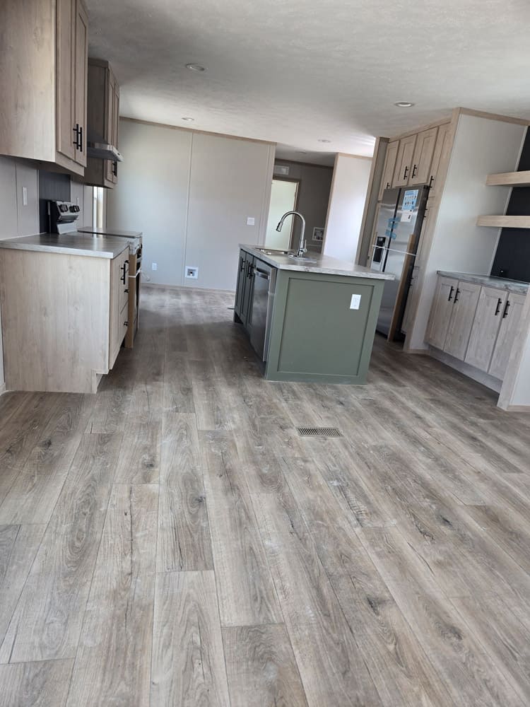 Open kitchen with green island and wood-look flooring in the Clayton Epic Hudson home in El Paso