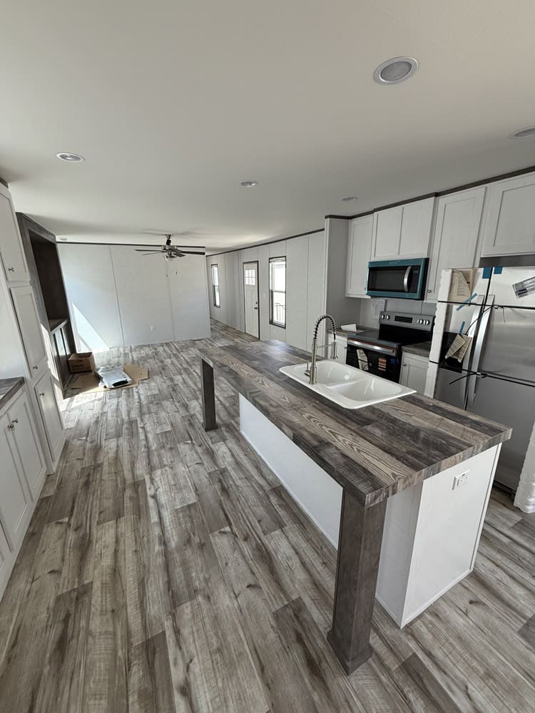 Kitchen island sink, white cabinets and stainless appliances in the Jessup Jackson 16x76 home in El Paso