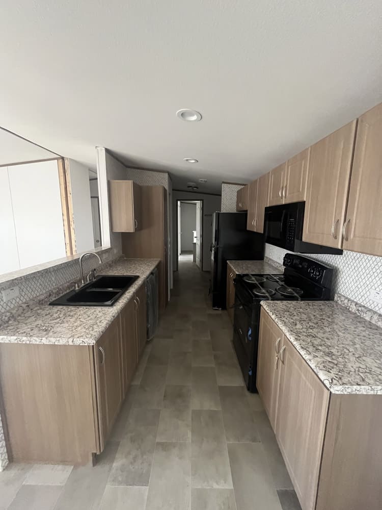 Galley kitchen with wood-tone cabinets and black appliances in the Legacy S-2468-42A home in El Paso