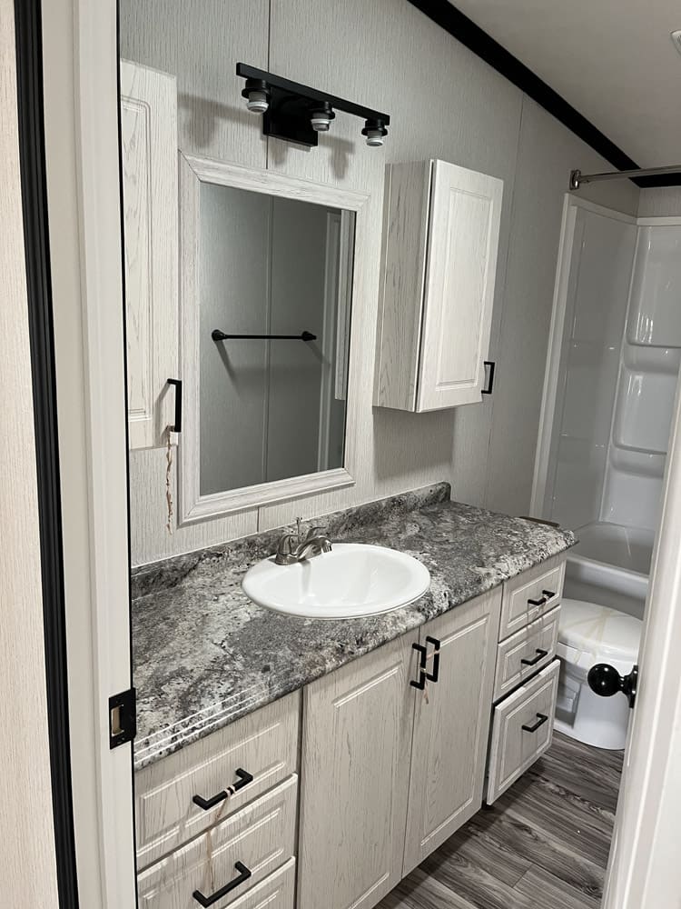 Single bathroom vanity and mirror with tub beyond in the Legacy C-3256-32B home in El Paso