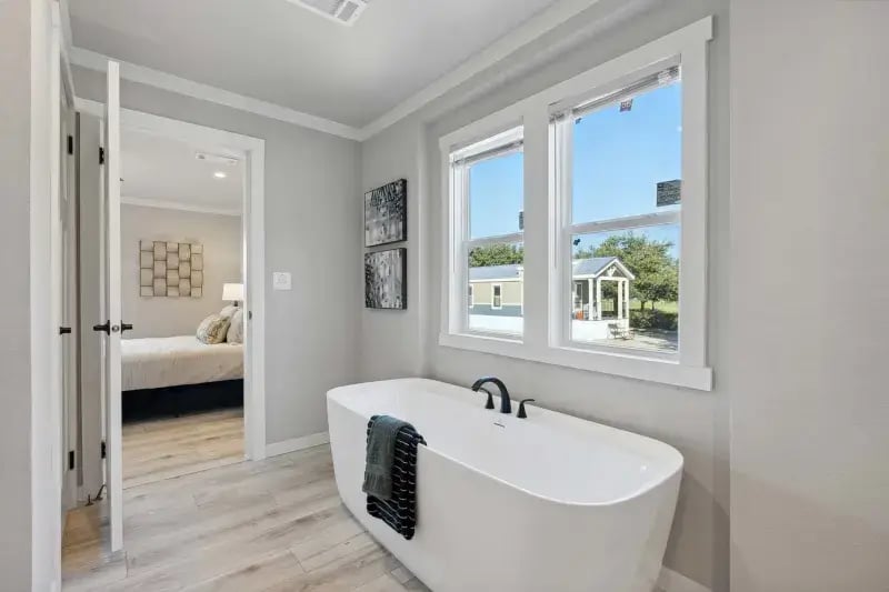 Freestanding soaking tub beneath two windows in The Carol primary bathroom