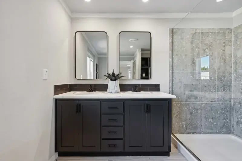 Dual-sink primary bathroom vanity and glass shower in The Carol by Champion Homes