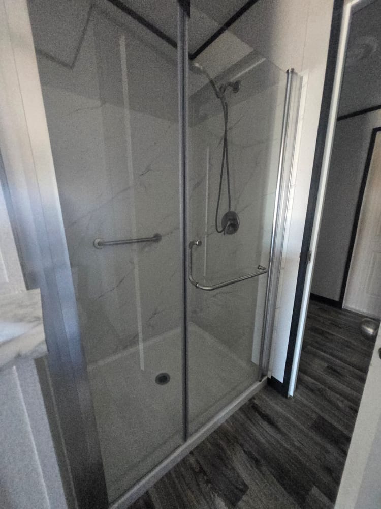 Glass shower enclosure with handheld showerhead in Legacy Housing H-3248-32A 32x48 home #5868 at New Start Homes in El Paso, TX