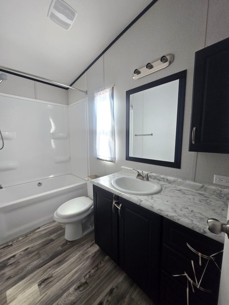 Bathroom vanity, framed mirror and tub-shower combination in Legacy Housing H-3248-32A 32x48 home #5868 at New Start Homes in El Paso, TX