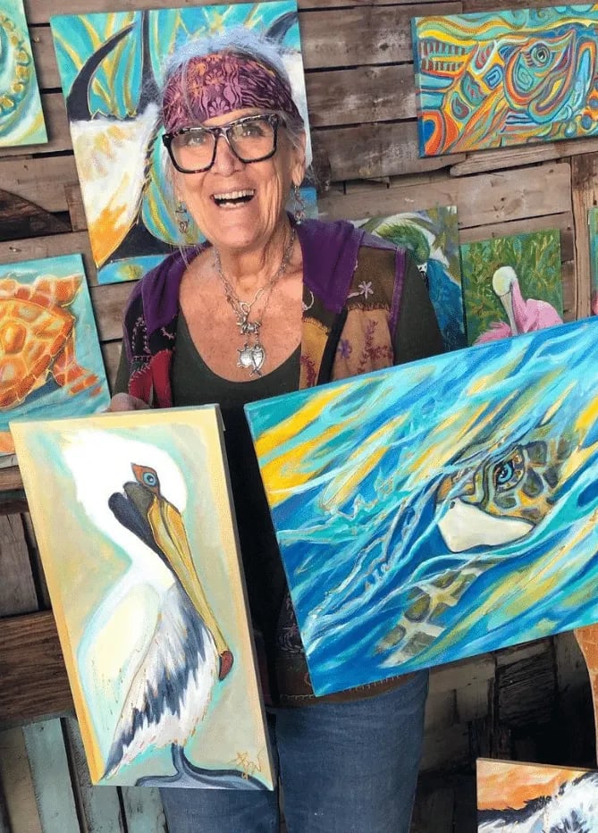 Barbara Weingardt holding her paintings of a pelican and a sea turtle