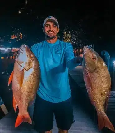 Man holding two fish from a night party boat trip