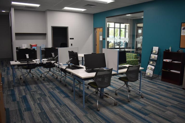 A modern office space with desks, computers, chairs, and a bookshelf against a blue and gray wall.