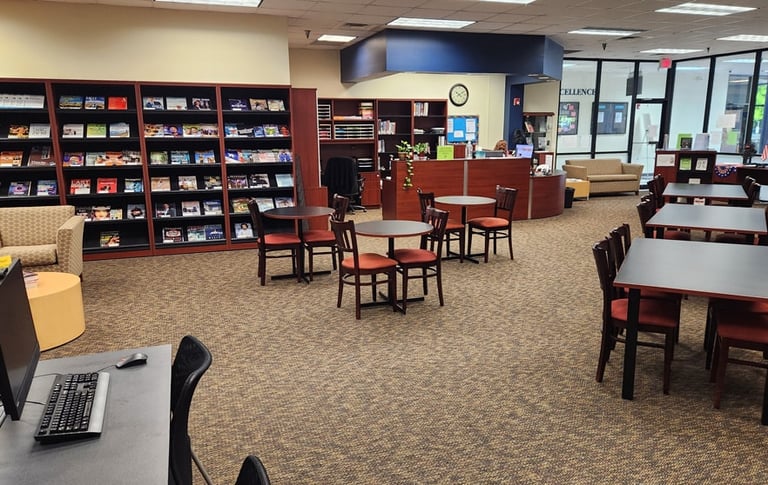 A library with bookshelves, tables, chairs, a computer, and a reception desk.