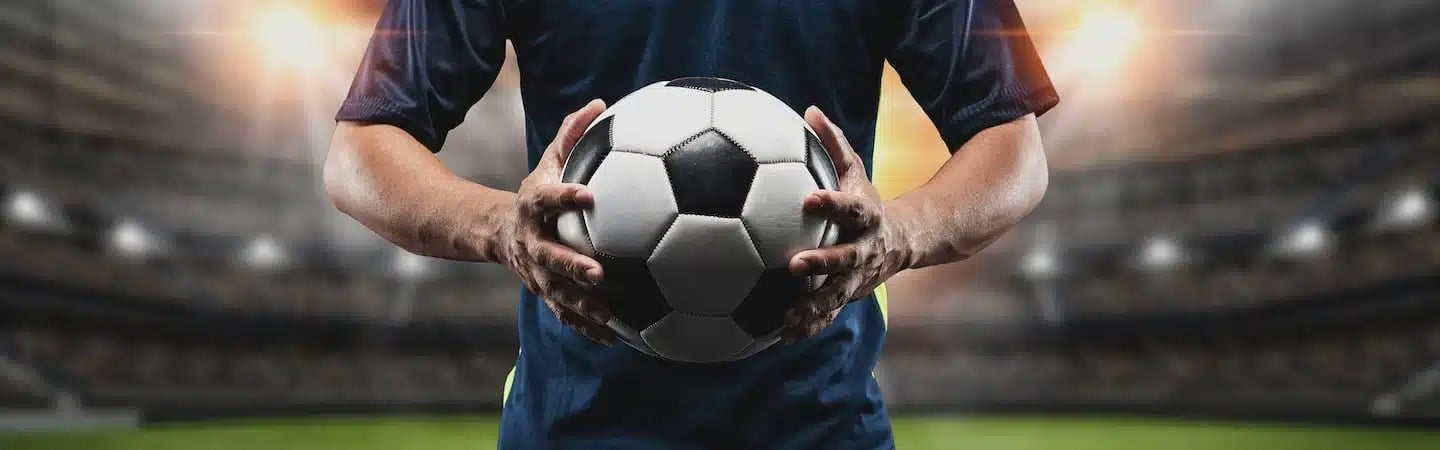 A soccer player holding a soccer ball in a brightly lit stadium, ready for the match.