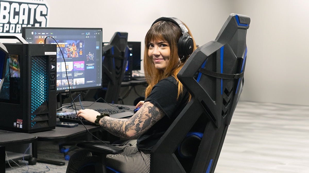Person with headphones smiling at a computer desk in a gaming setup.