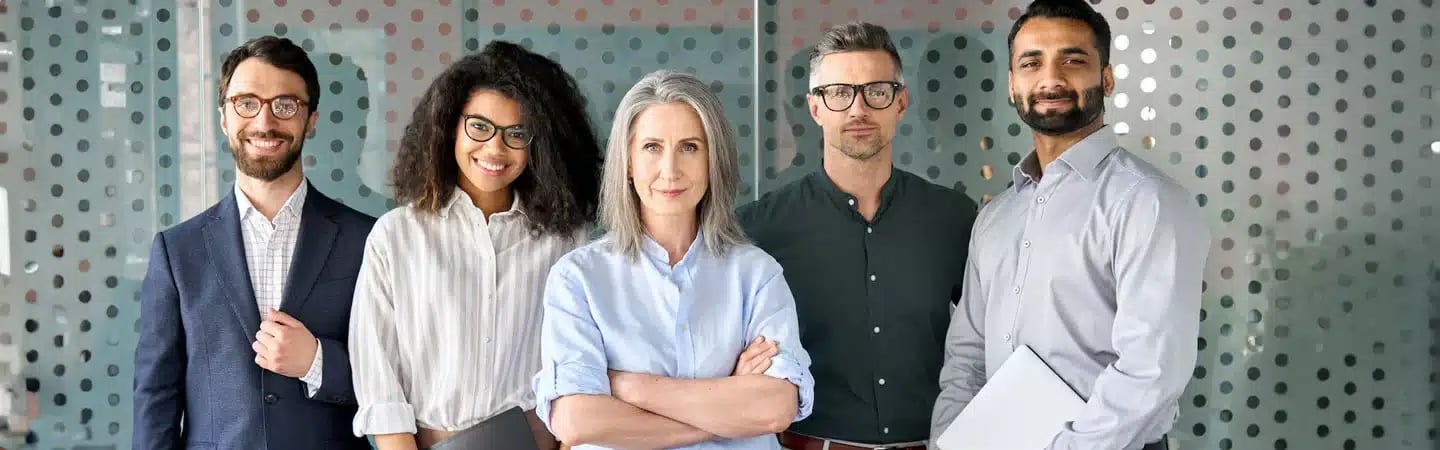 A diverse group of five professionals, three men and two women, standing together in an office setting.