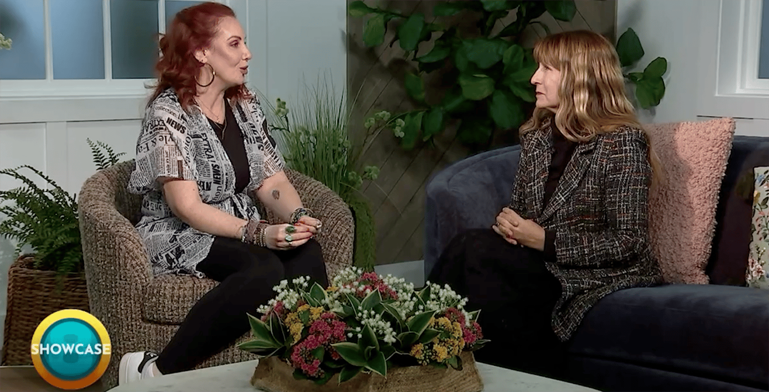 Two women sit facing each other in a cozy, well-lit living room, chatting about the upcoming Spring Semester at Bryant & Stratton College. A round table with a floral arrangement separates them, and a “SHOWCASE” logo appears in the bottom left corner.