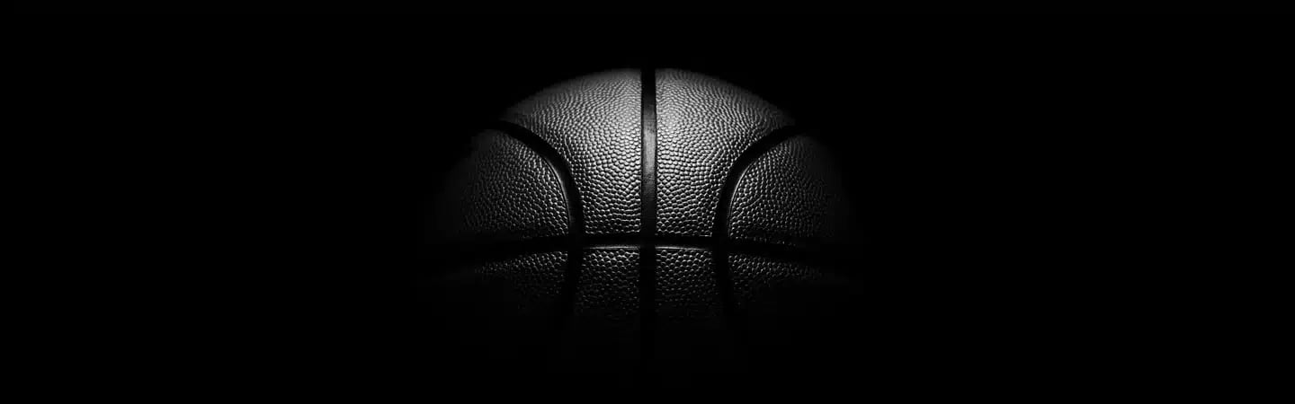 A basketball partially illuminated from above, set against a dark, shadowy background.