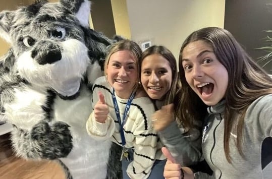 Three people smiling and giving thumbs up with a person in a furry animal costume standing beside them.