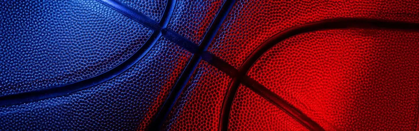 Close-up of a basketball with a pattern of pebbled leather, dramatically lit with blue and red lighting.