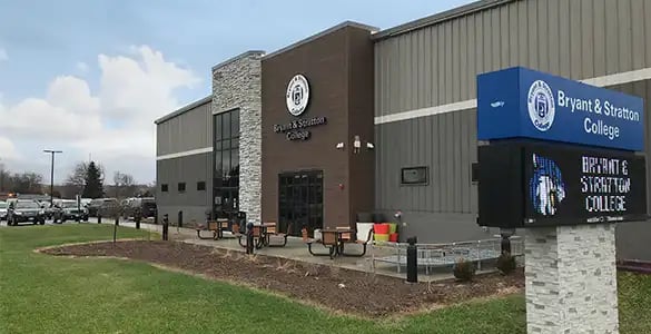 Exterior view of Bryant & Stratton College building with entrance and electronic sign in the foreground.