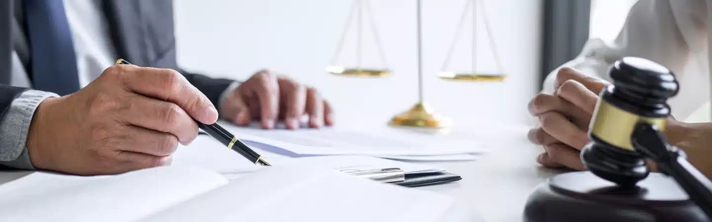 Two people discussing legal documents at a desk with a gavel and scales of justice in the background.