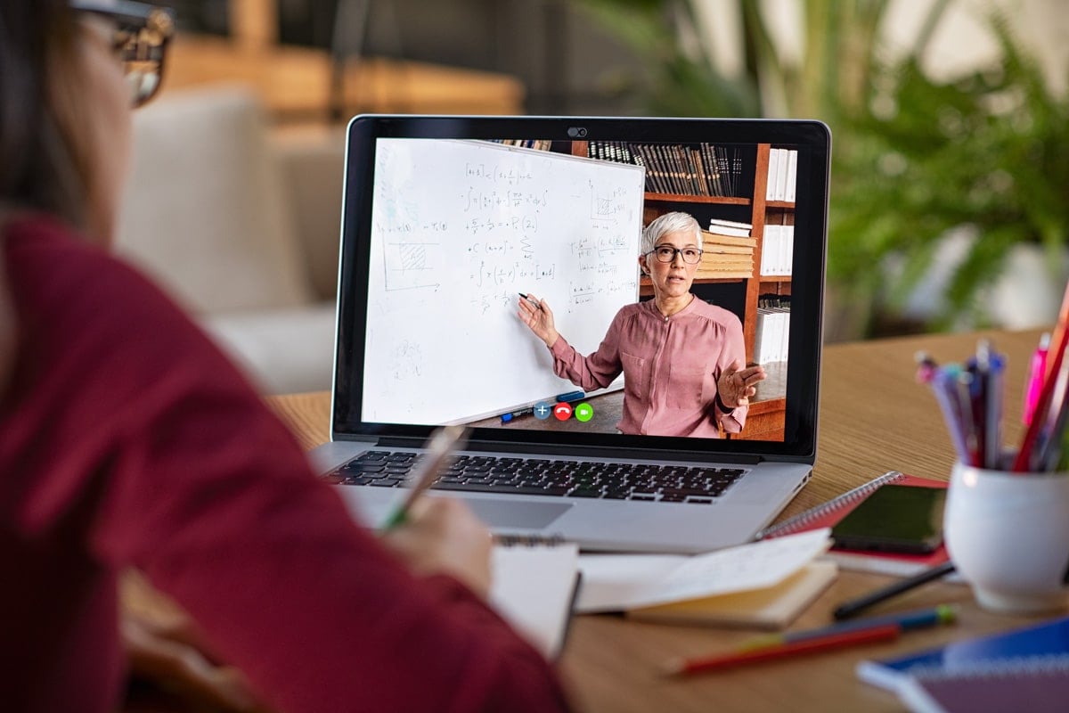 Person attending an online class, watching an instructor explain math concepts on a whiteboard via a laptop.
