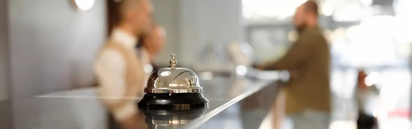 Close-up of a hotel bell on a counter with two blurred people talking in the background.