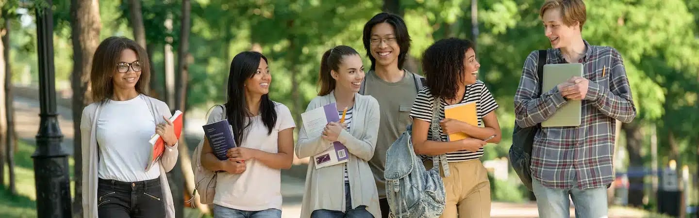 A group of six diverse students walking outside with books and backpacks, smiling and talking to each other.