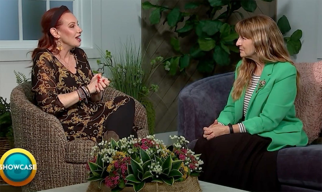 Two women sit facing each other in a studio setting, engaged in conversation about Stackable Degrees. One wears a black patterned dress, the other a green blazer. A floral centerpiece is on the table. “SHOWCASE” and Bryant & Stratton College appear in the corner.