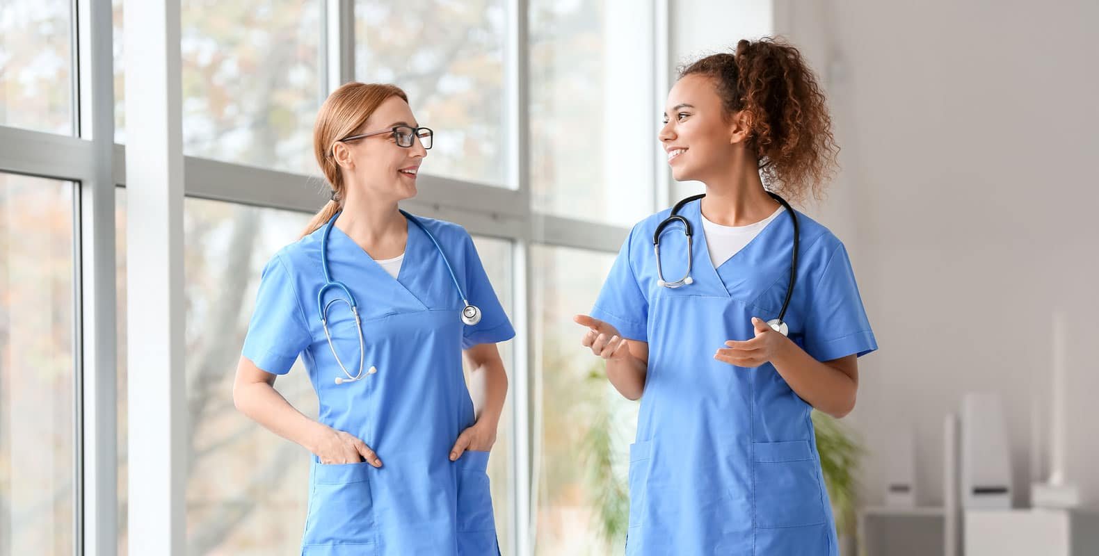 Two nurses in blue scrubs engage in a friendly conversation, representing the importance of understanding nursing laws and regulations to provide ethical and responsible care.