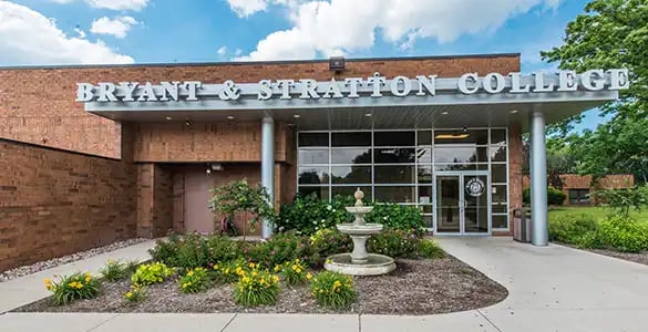 Entrance of Bryant & Stratton College with a garden and fountain in front, and a modern building under a blue sky.