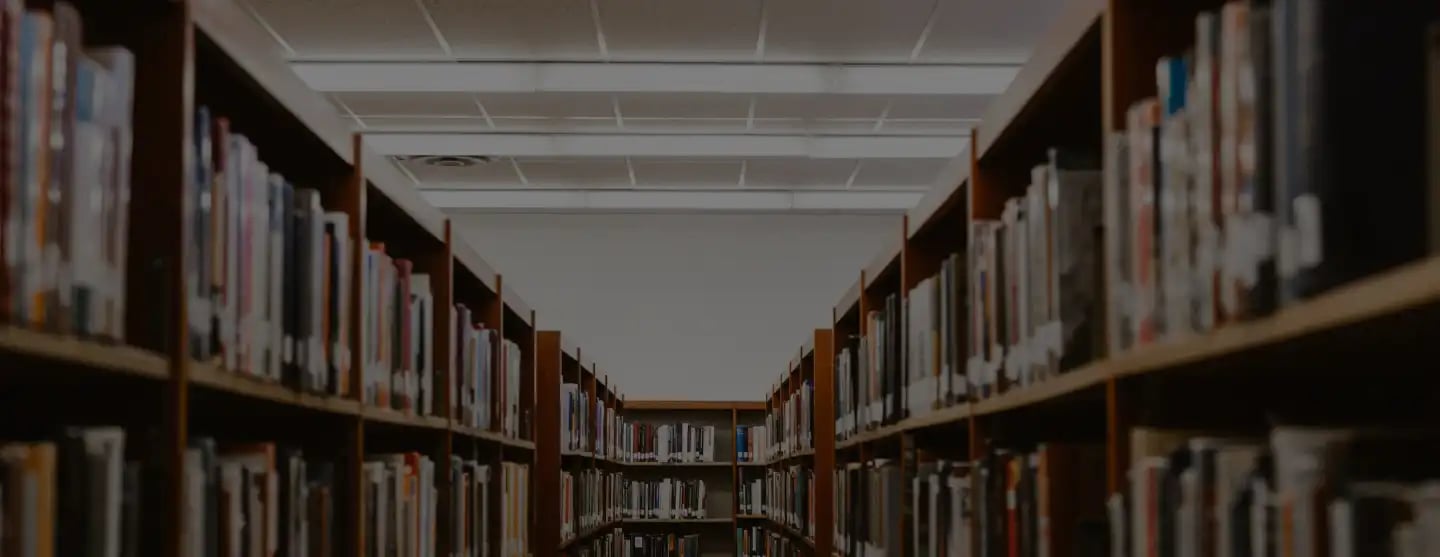 A dimly lit library aisle with bookshelves full of books on both sides.