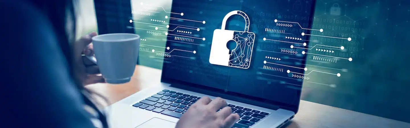 Person holding a mug and typing on a laptop with a padlock icon on the screen, symbolizing cybersecurity.