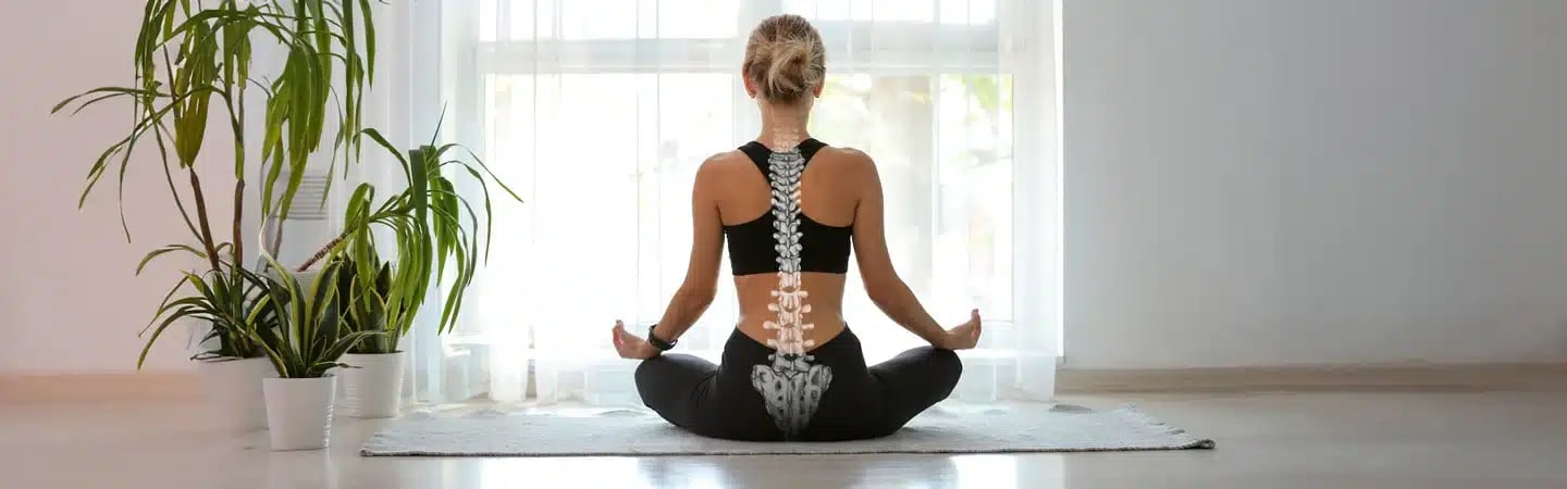 Woman in black sportswear practicing yoga, sitting cross-legged with a superimposed image of a spine on her back.