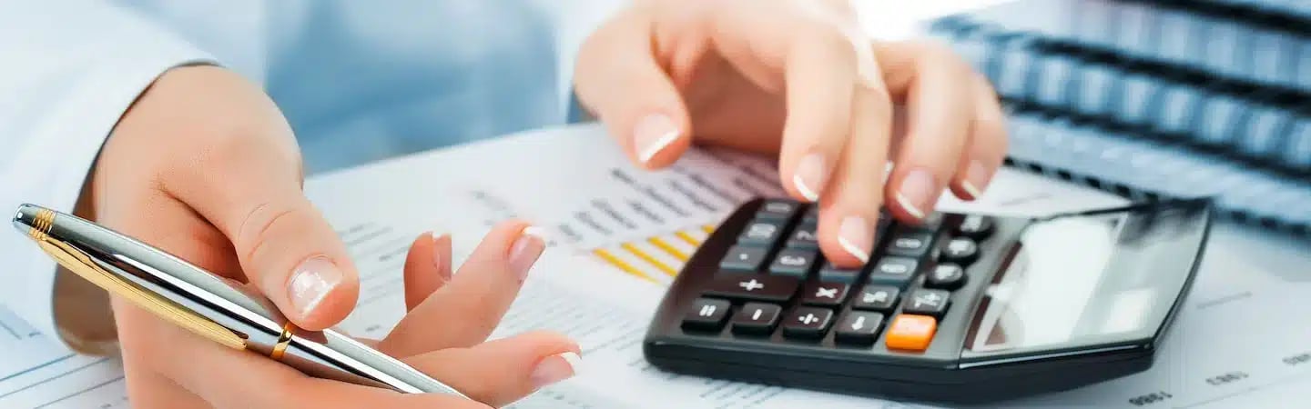 Hands using a calculator and holding a pen while analyzing financial documents.