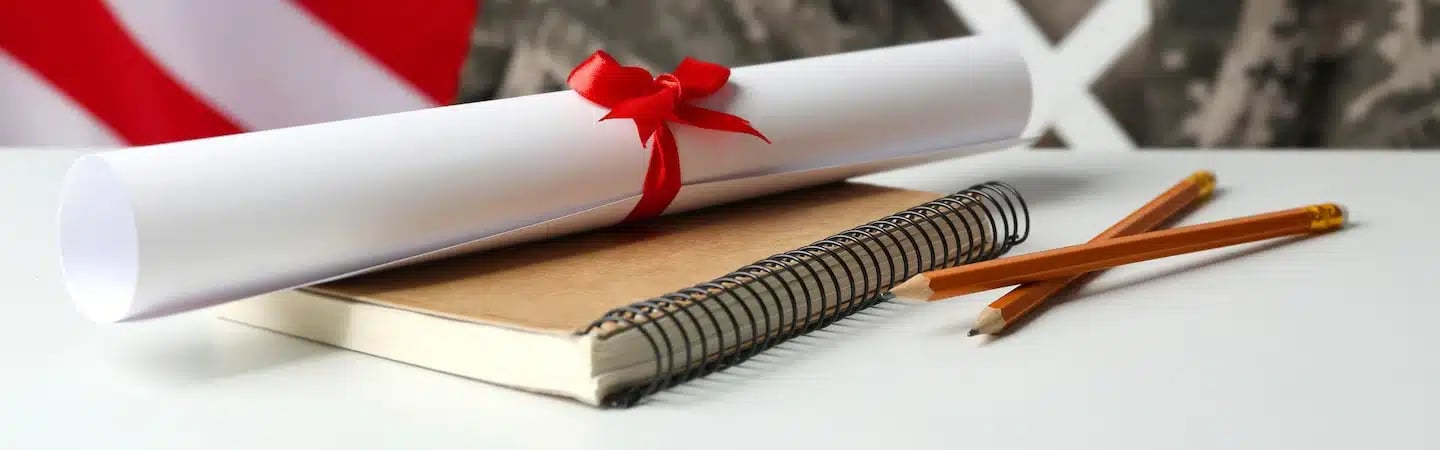Rolled certificate with red ribbon, notebook, and two pencils on a white surface with a blurred background.