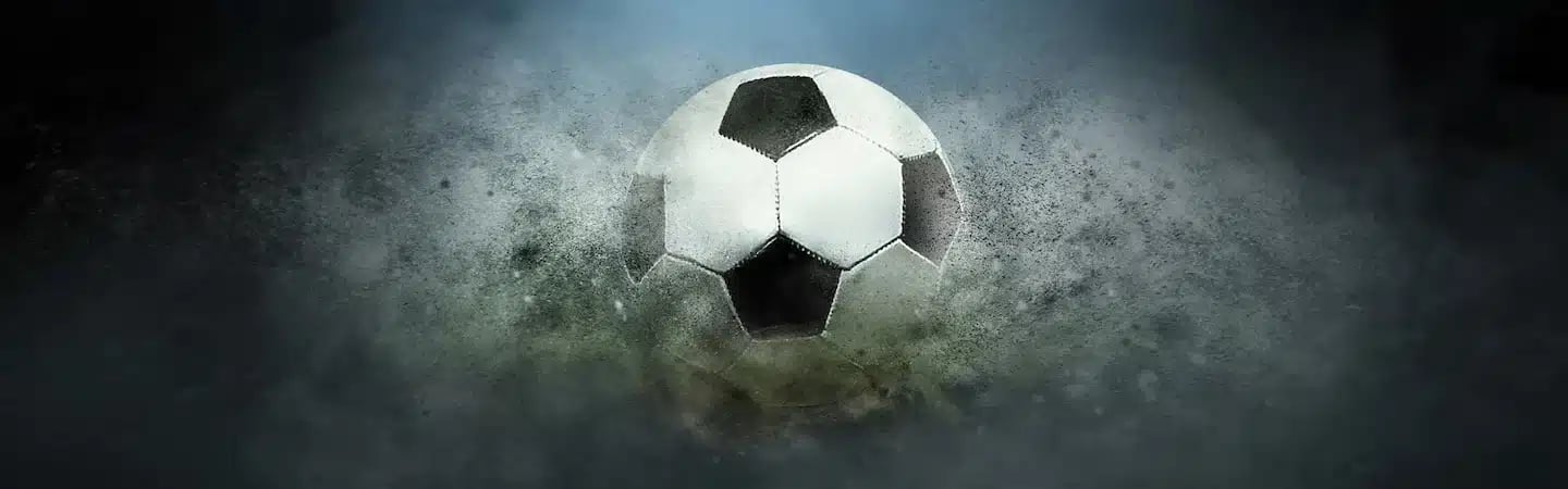 A soccer ball in mid-air surrounded by a cloud of dust or smoke against a dark, misty background.