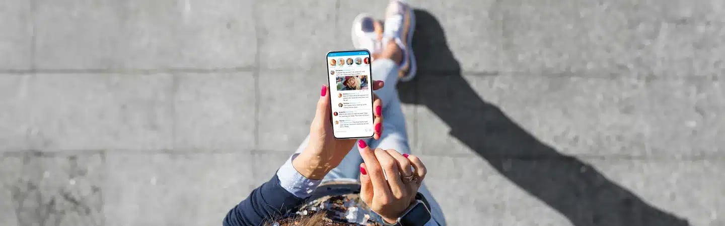 Person with red nails holds phone displaying social media feed while standing on grey pavement.