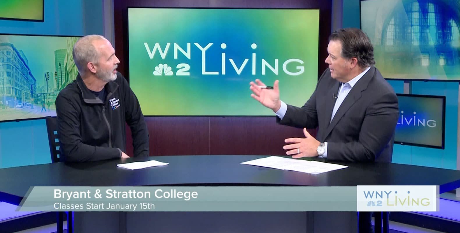 Jeff Tredo sits at a news studio desk during a WNY Living segment discussing Bryant & Stratton College classes starting January 15th.