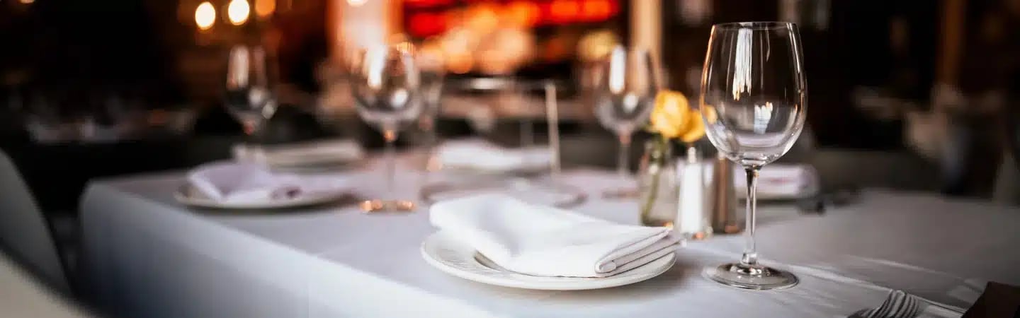 Elegant restaurant table setting with white tablecloth, wine glasses, and neatly folded napkins.