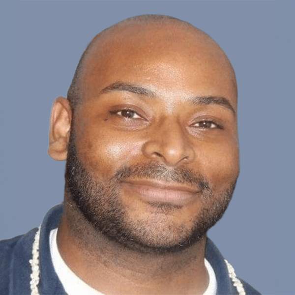 A man with a bald head and beard smiling against a blue background.