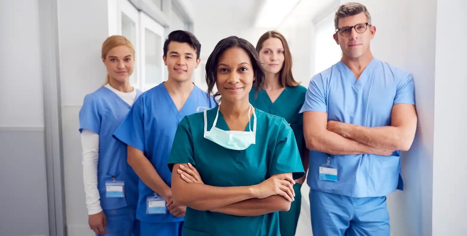 Group of healthcare professionals in scrubs standing confidently in a hospital hallway.